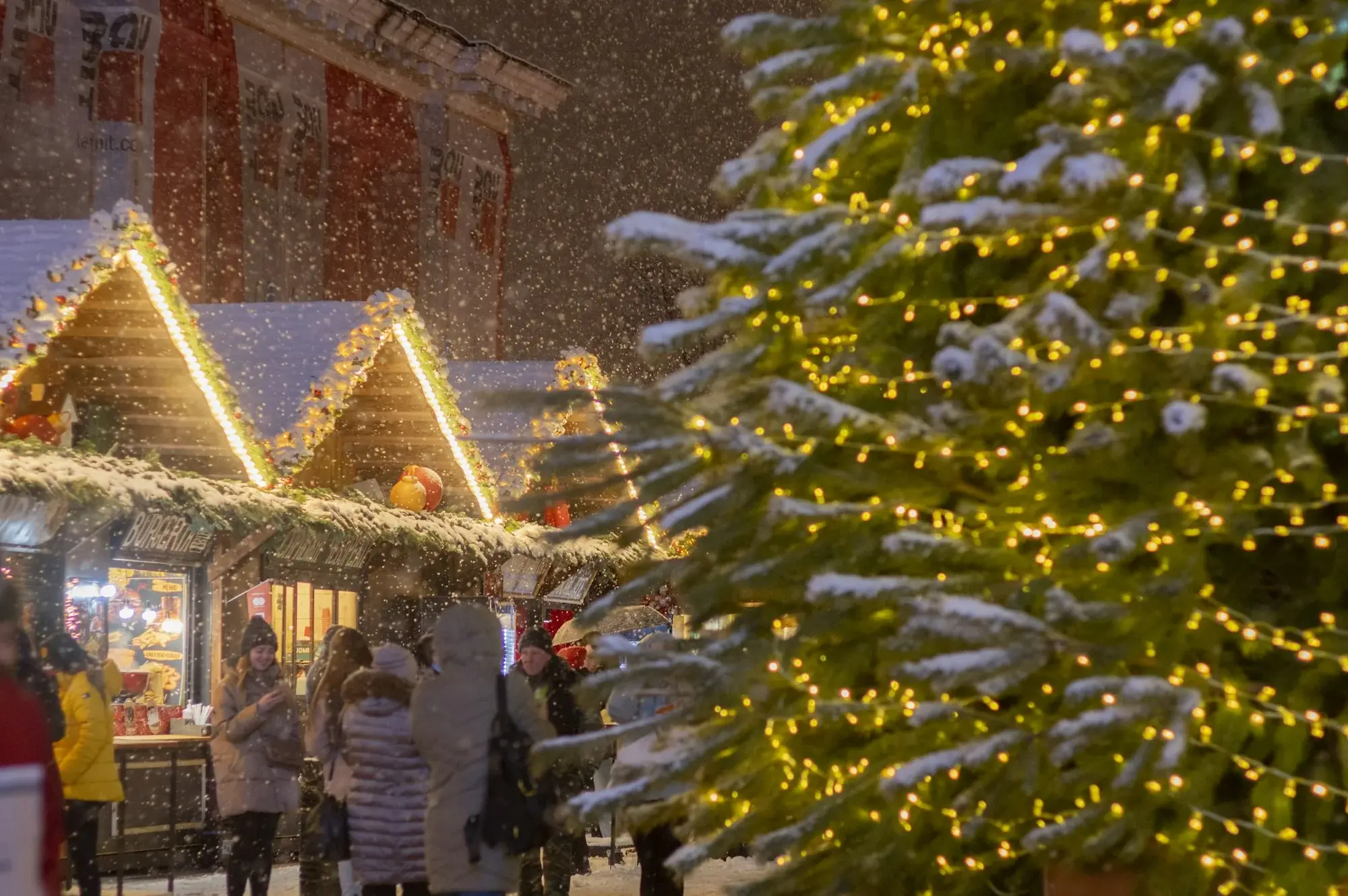 Julmarknad i snöfall med upplysta stånd och en gran